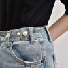 Close-up of a person wearing denim jeans with a pearl brooch detail on the pocket