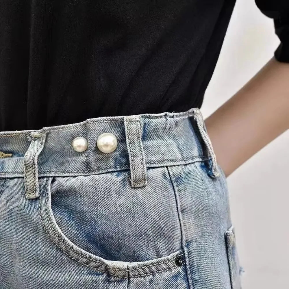 Close-up of a person wearing denim jeans with a pearl brooch detail on the pocket