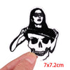 Black embroidery patch featuring a skull design with a female face and hair, shown being held by a hand.