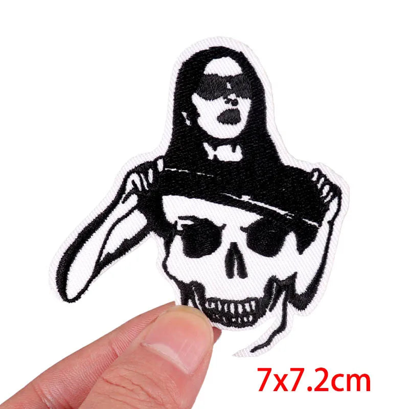 Black embroidery patch featuring a skull design with a female face and hair, shown being held by a hand.