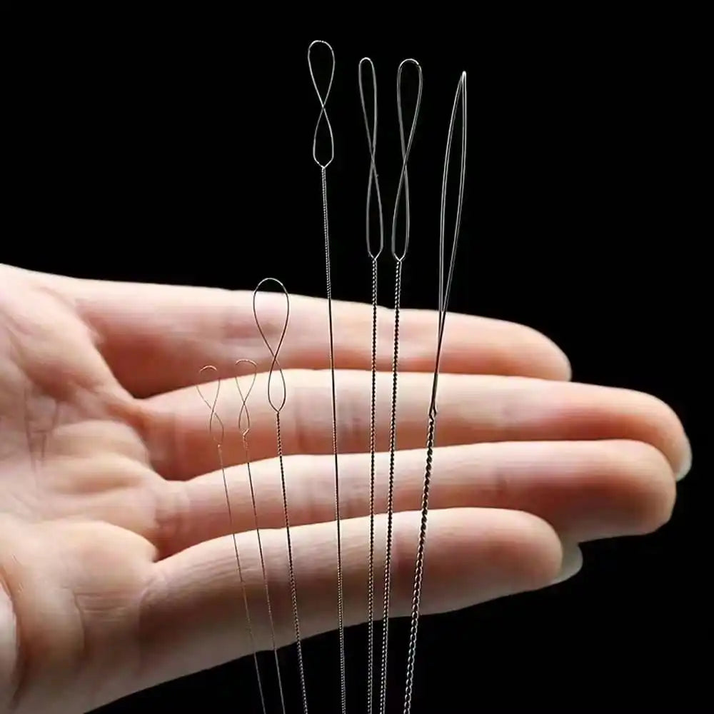 A hand holds a set of fine, silver-colored precision beading needles for jewelry making.