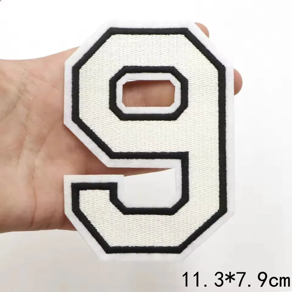 A white and black letter patch shaped like the number 9 is held in a hand.
