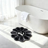 A black gothic sunflower absorbent non-slip bathroom mat placed on a white marble floor near a modern white bathtub.