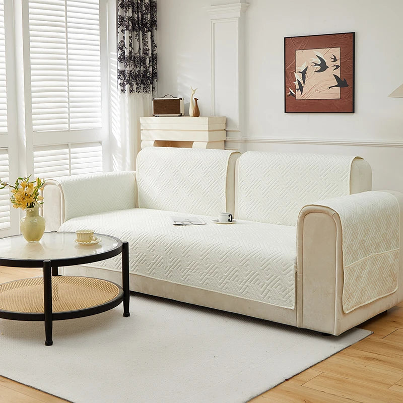 A cream-colored geometric quilted sofa cushion cover displayed on a light-colored sofa in a bright room.
