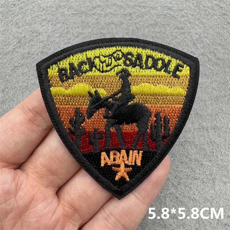 Black embroidered patch featuring a silhouette of a cowboy riding a saddle and the text BACK THE SADDLE ABAIN