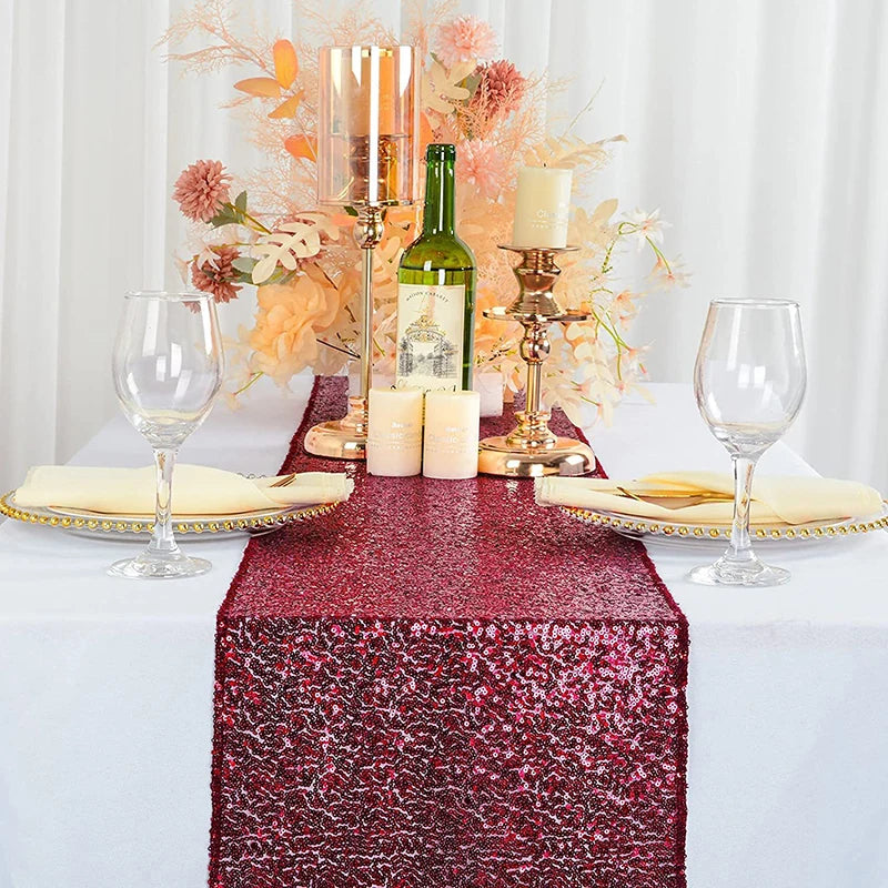 A red sequin table runner with gold accents, candles, and floral decor set on a white tablecloth.