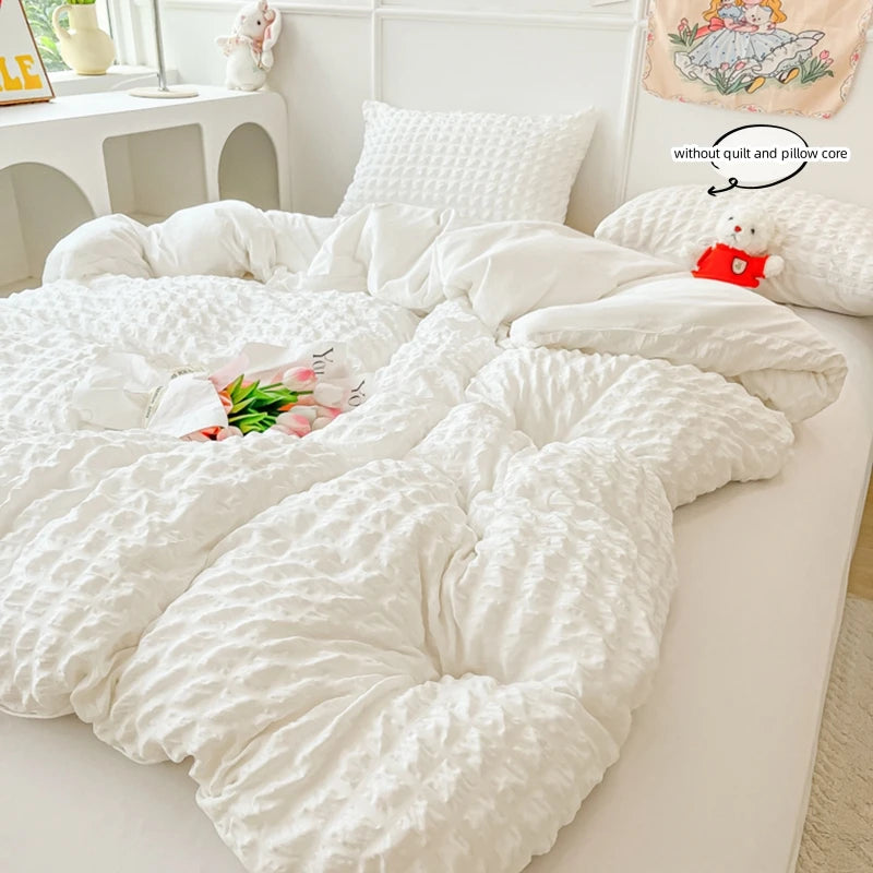A white quilted duvet cover and pillow set displayed on a bed, with a small stuffed animal nearby.