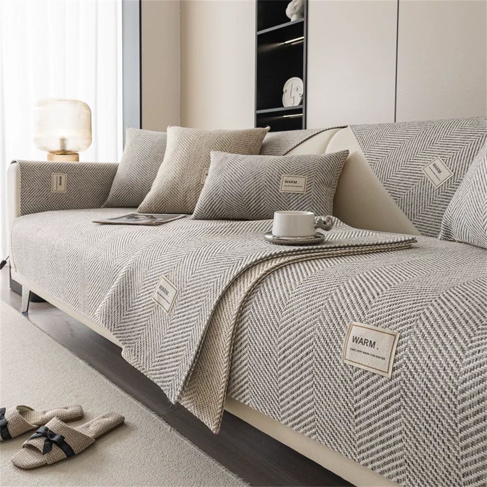 A beige anti-slip sofa cover draped over a light-colored sofa with neutral pillows and a textured throw.