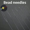 A collection of silver bead needles and a small yellow bead are displayed on a dark surface.