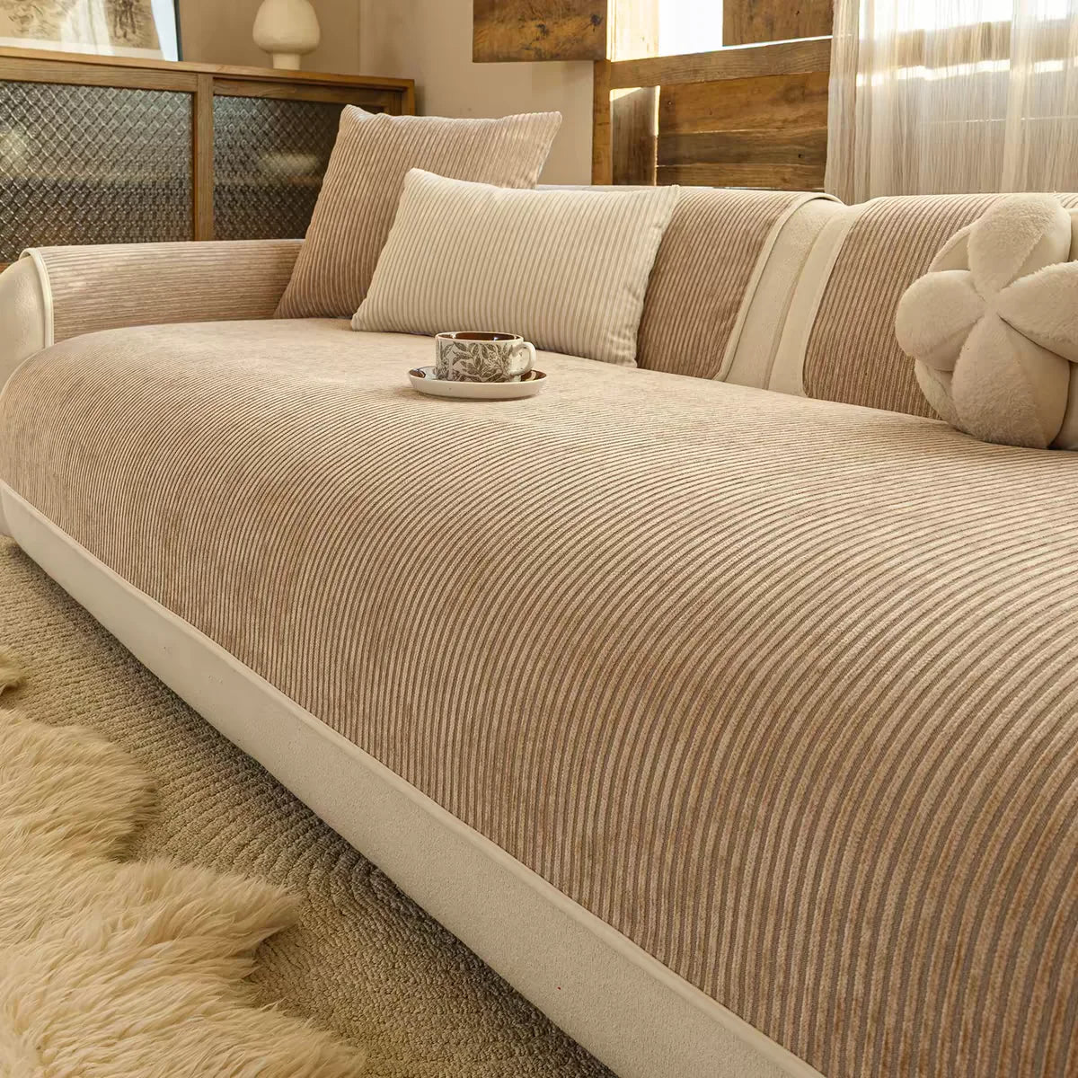 A beige striped chenille sofa cover displayed on a light-colored sofa with natural wood accents and sheer curtains.