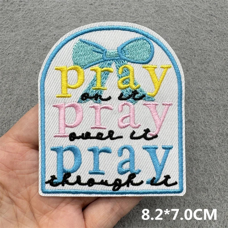 A light blue embroidered patch with the text Pray on it pray over it pray through it in yellow and pink thread.