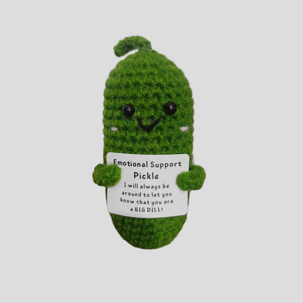 A handmade plush pocket doll shaped like a green pickle with a smiling face and an emotional support message tag.