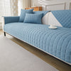 A light blue quilted anti-slip sofa cover with a plush texture on a white sofa.