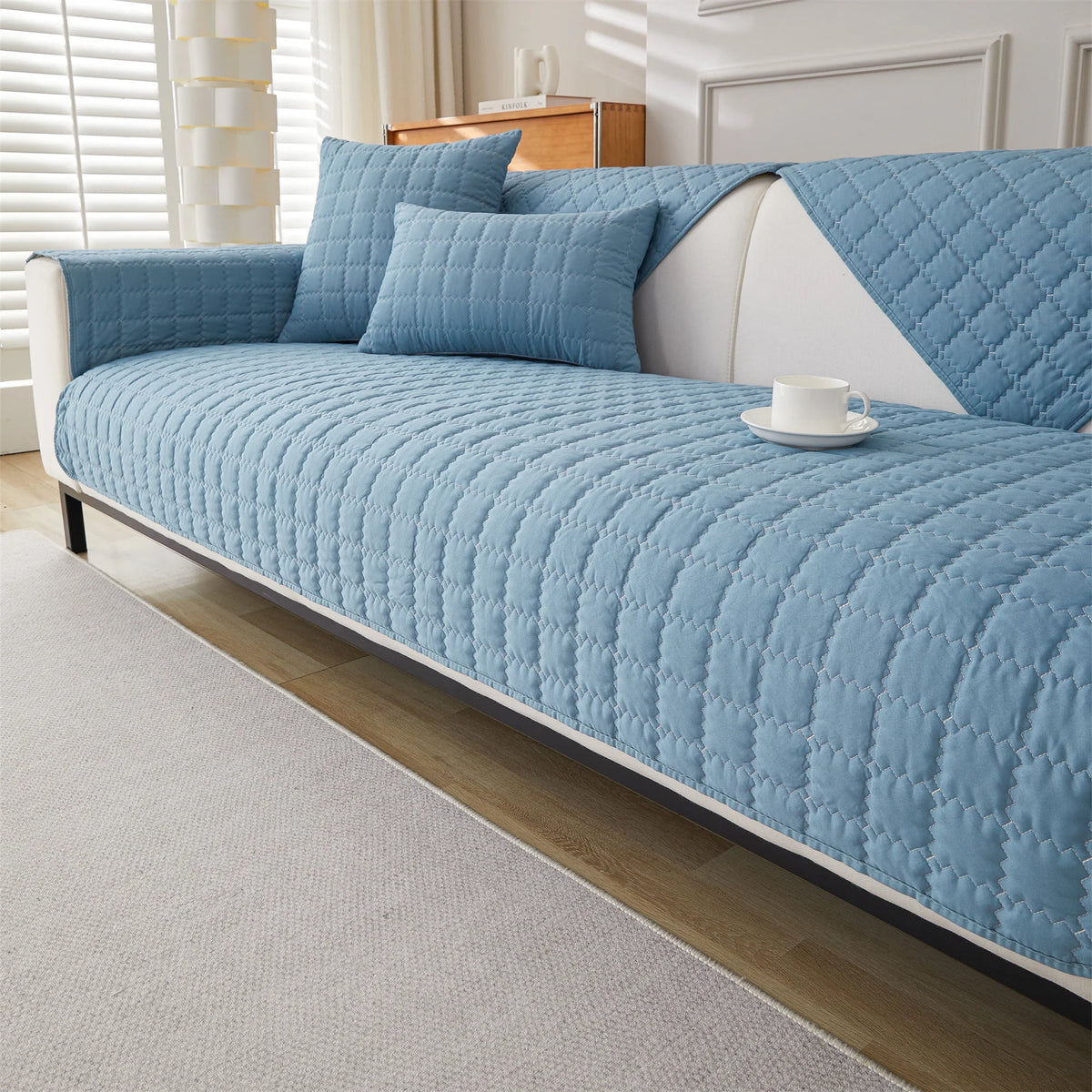 A light blue quilted anti-slip sofa cover with a plush texture on a white sofa.