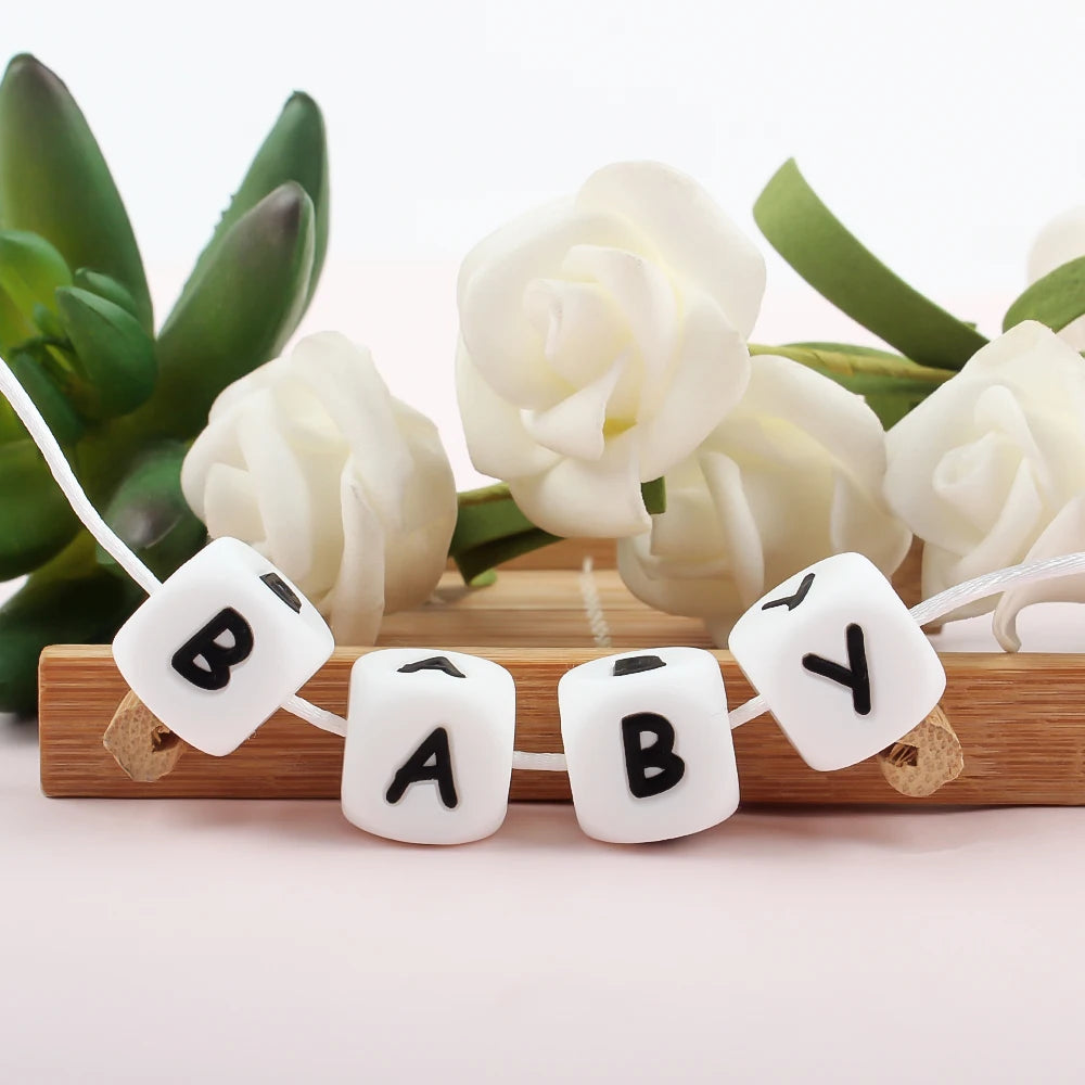 White silicone alphabet beads spelling BABY strung on a string with white roses and green leaves