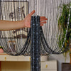 A hand is pulling a black beaded string curtain with silver tassels down, showing the sheer fabric texture.