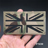 A black tactical flag patch featuring a distressed camouflage pattern on a beige fabric, held in a hand.