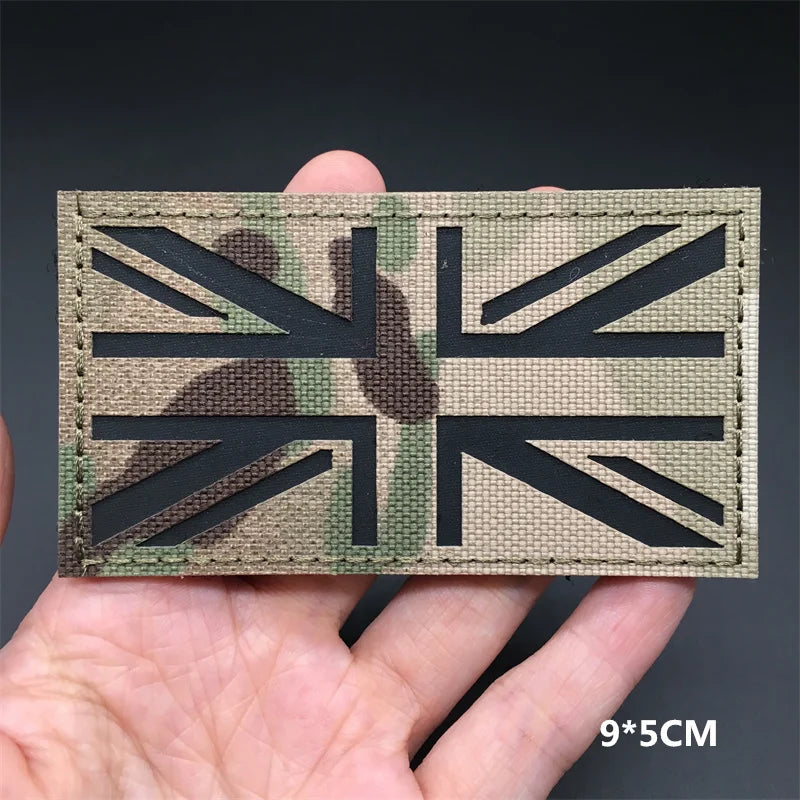 A black tactical flag patch featuring a distressed camouflage pattern on a beige fabric, held in a hand.