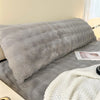 A gray plush long pillowcase resting on a bed, with a white knitted blanket nearby.
