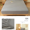 A gray fitted sheet set with pillowcases displayed on a wooden bed frame in a bright bedroom setting.