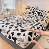 A black and white cow print fitted sheet is being handled on a bed.