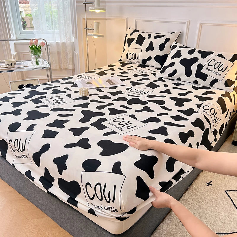 A black and white cow print fitted sheet is being handled on a bed.