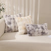 A collection of fluffy faux rabbit fur decorative throw pillows in shades of white and gray resting on a light-colored sofa.