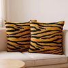 Two throw pillows with an orange and black leopard print pattern resting on a light-colored sofa.