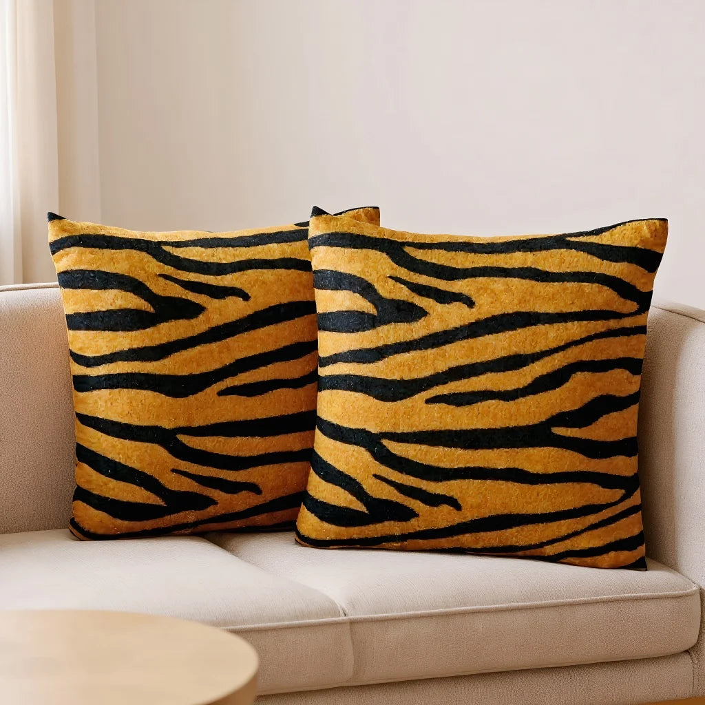 Two throw pillows with an orange and black leopard print pattern resting on a light-colored sofa.