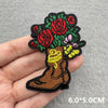 Embroidered patch of a cowboy boot featuring a tree of red and pink roses on a gray background.