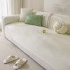 A light cream sofa slipcover with green accent pillows and white anti-slip slippers on the floor.