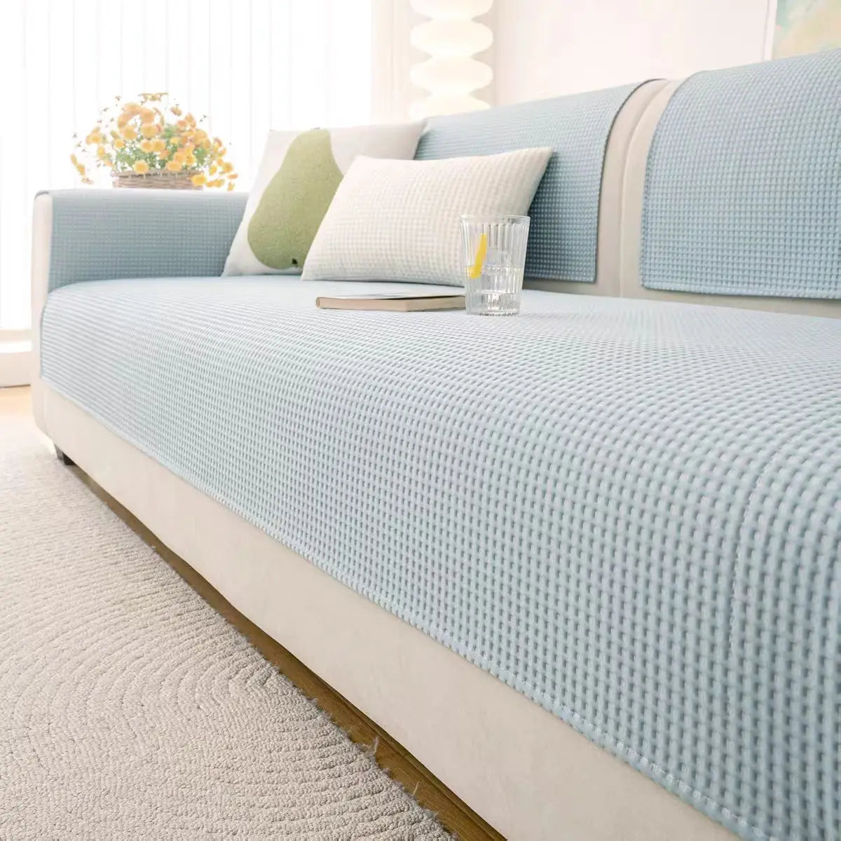 A light blue machine washable anti-slip sofa slipcover with white pillows and a light rug.