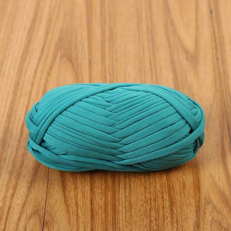 A ball of teal flat thread yarn for crafting and sewing resting on a wooden surface.