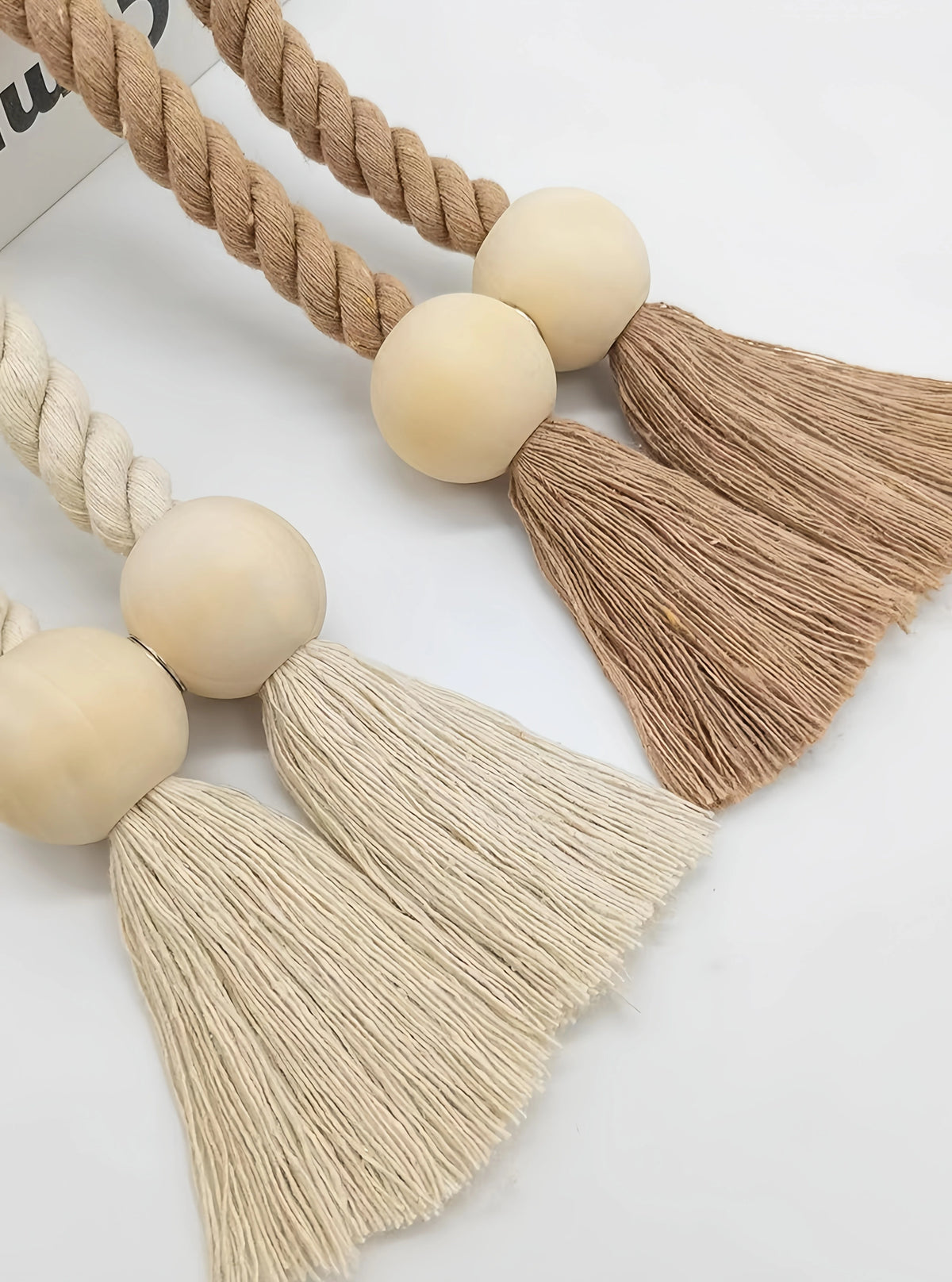 Two hand-woven wooden curtain tiebacks in natural beige and cream tones displayed on a white background.