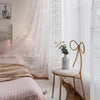 White sheer curtains with floral embroidery hanging in a bright bedroom setting