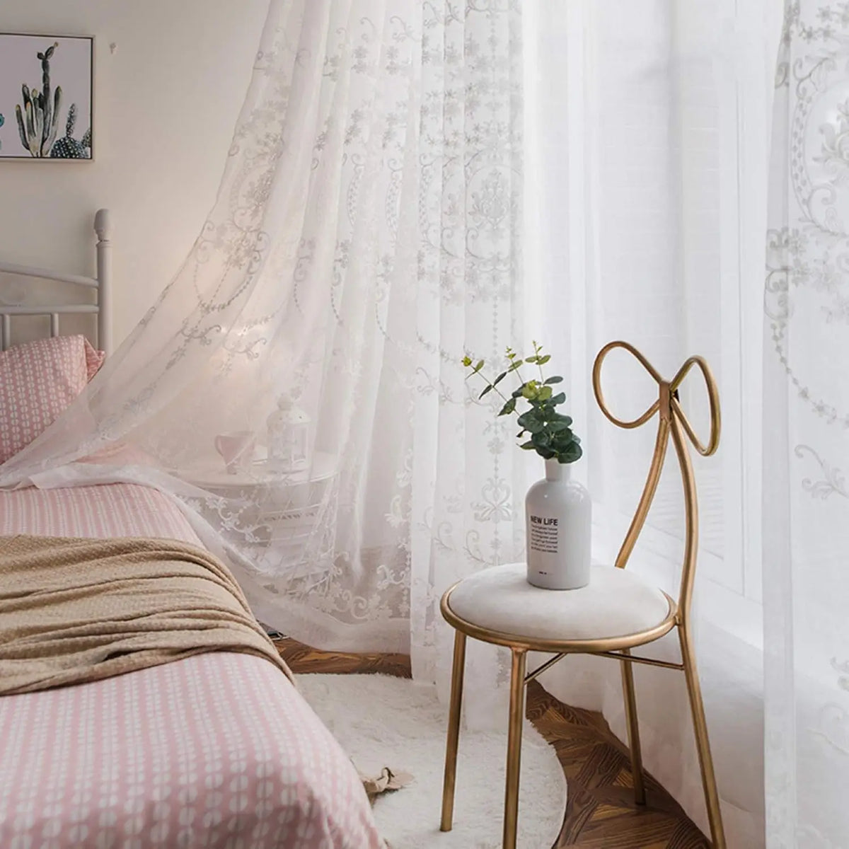 White sheer curtains with floral embroidery hanging in a bright bedroom setting