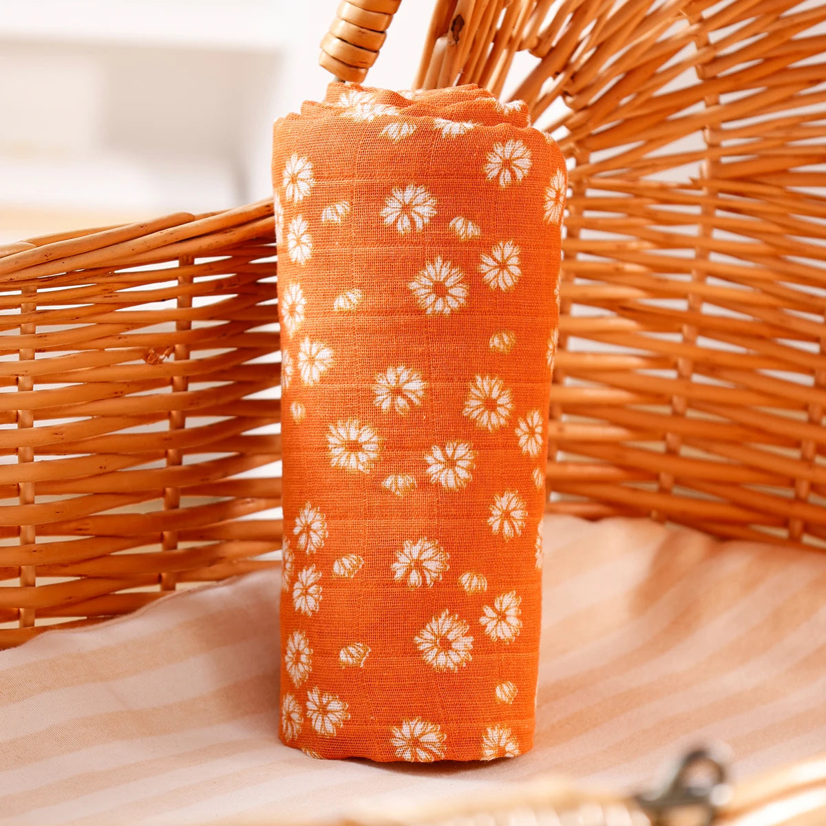 Orange cotton muslin swaddle blanket rolled up, resting on a woven basket.