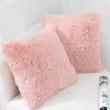 A square, fluffy pink velvet throw pillow resting on a white surface.