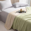A light green ice silk cooling comforter is displayed on a white bed with white pillows.