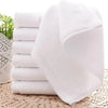 A stack of white cotton face towels is displayed on a woven mat next to some greenery.