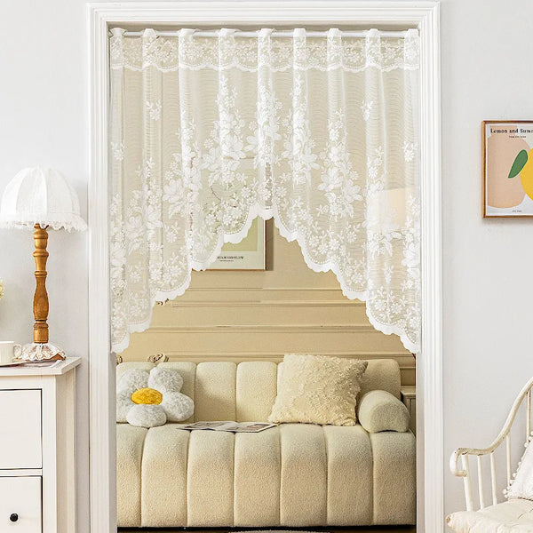 A sheer floral curtain valance in cream fabric hangs over a light-colored sofa.