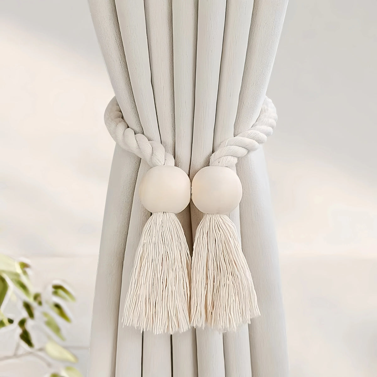 Hand-woven wooden curtain tiebacks with cream tassels tied on a light beige fabric drape