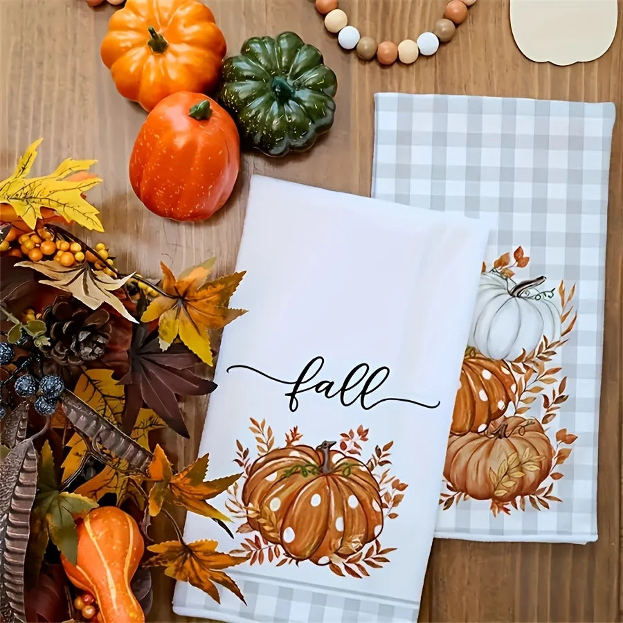 A kitchen towel featuring an autumn pumpkin print with leaves and acorns, set against a wooden background.
