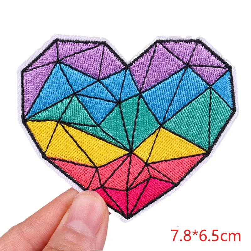 A heart-shaped embroidered patch featuring a colorful, geometric design with shades of blue, purple, green, yellow, and pink.