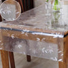 A transparent PVC tablecloth with a floral pattern covers a wooden table.