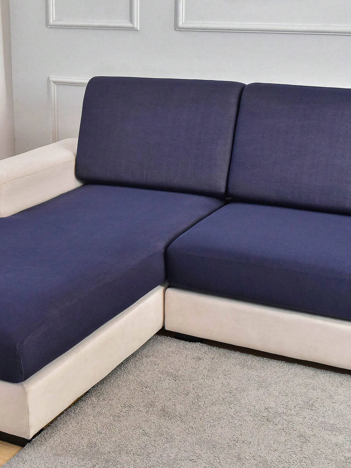 A modern sofa with dark blue slipcovers and light cream trim resting on a beige carpet.