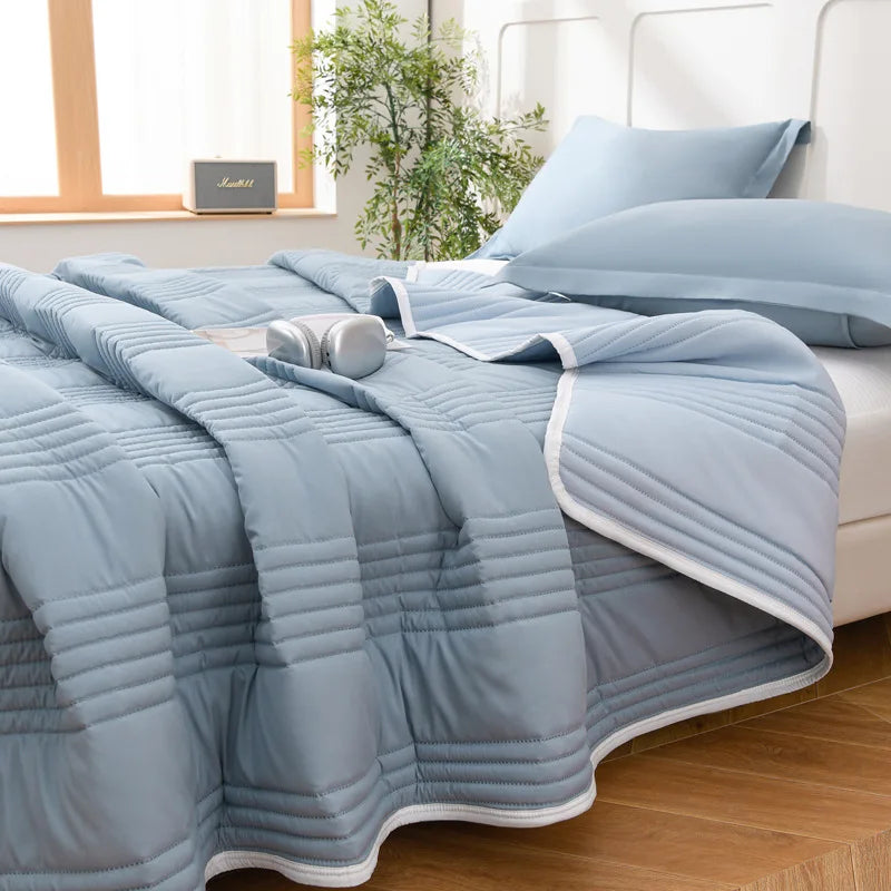 Light blue quilted blanket spread over a bed with pillows and a window in the background.