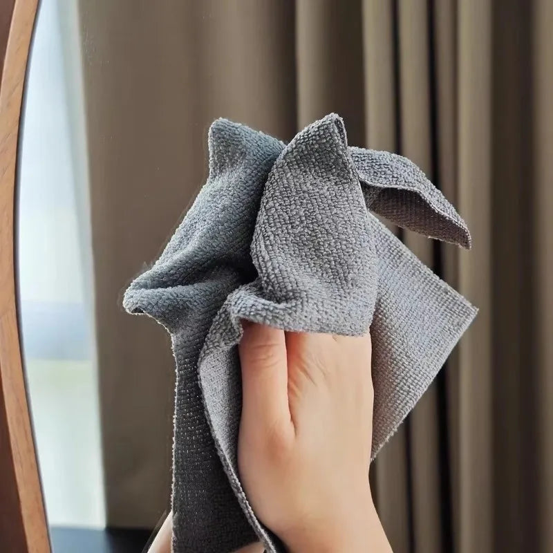 A hand is folding a gray reusable microfiber cleaning wipe, visible in a mirror reflection.