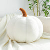 A white plush pumpkin decoration with a brown stem resting on a white knitted fabric.