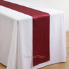 A white tablecloth with a deep burgundy satin table runner draped across it.